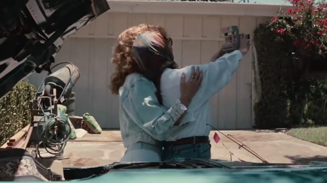 Thelma and Louise posing for a Polaroid camera outside a house in front of a car from the back