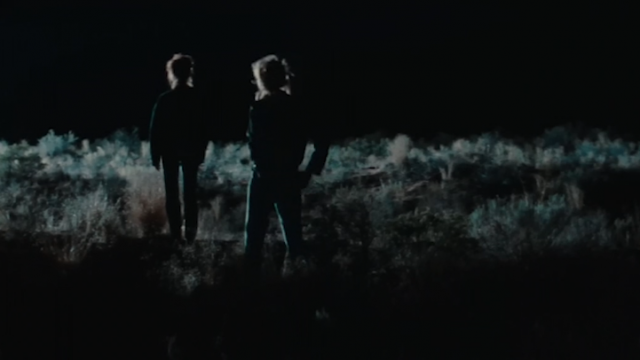 Thelma and Louise standing in the moonlight with their backs facing us