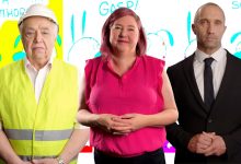 3 white people stand side by side: the first, an older man in a yellow construction vest and white hardhat, the second, a middle-aged woman in a pink shirt with flat pink hair, and the third a middle-aged bald man in a black suit and tie.