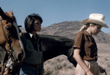 A brunette and a blonde woman in a cowboy hat walk with 2 horses in Nevada. From Desert Hearts.