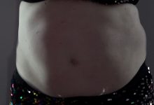 A white woman's belly fills the screen in low lighting